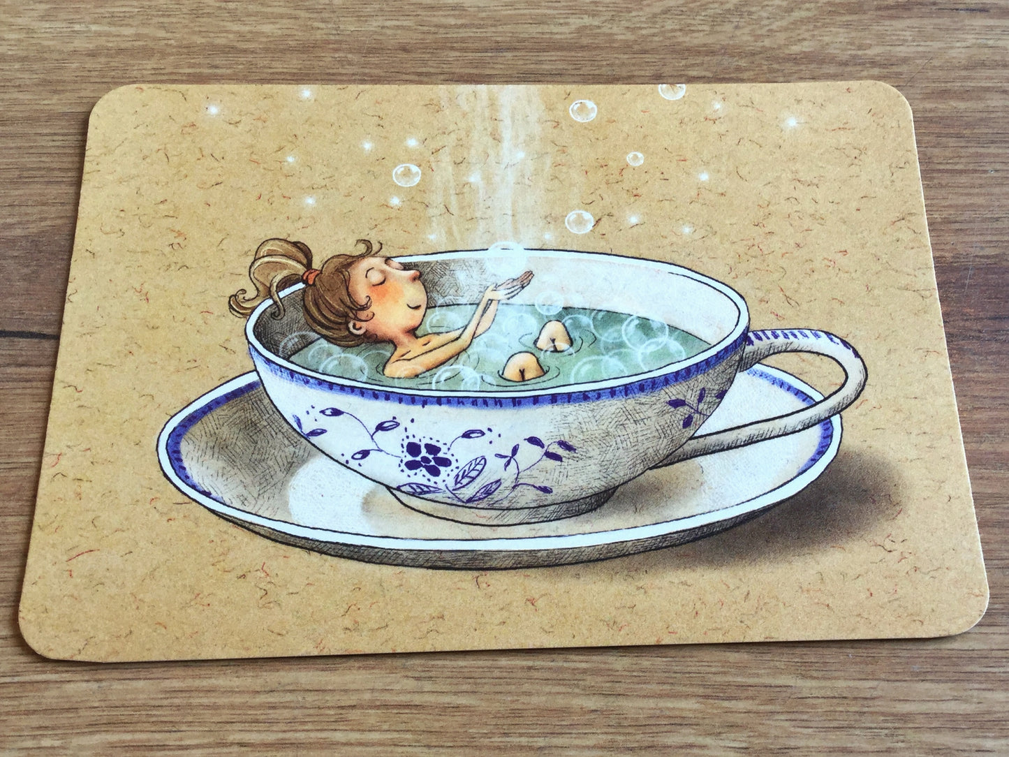 Die Postkarte zeigt eine blauweiß-geblümte Tasse mit dampfendem Tee, in dem ein Mädchen badet und mit Seifenblasen spielt. Gutrath-Verlag.
Erhältlich bei Polly Paper - Umweltfreundliche Schreibwaren in Berlin Mitte