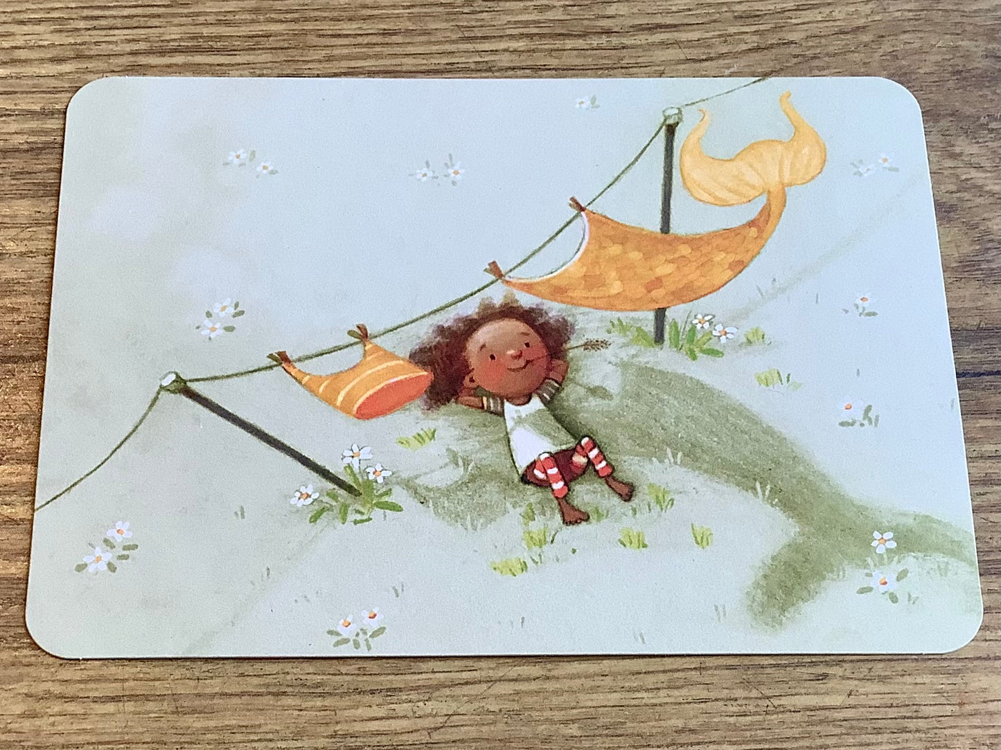 Postkarte: Kind liegt unter einer Wäscheleine mit Nixenkostüm und schaut in den Himmel