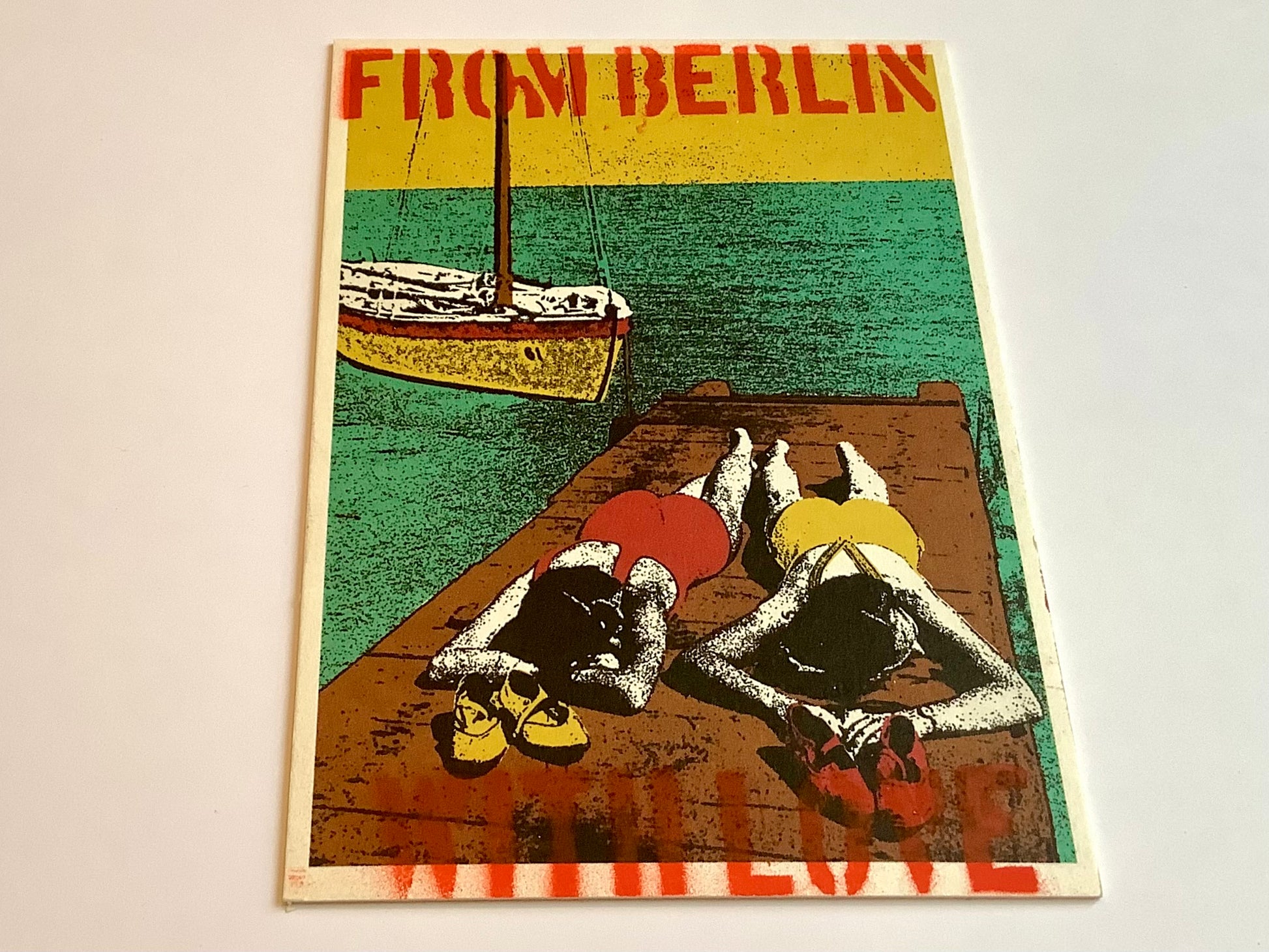 Die illustrierte Postkarte zeigt  2 Frauen im 20er-Jahre Badeanzug auf dem Bauch liegend auf einem Steg am Wasser, Boot im Hintergrund. Der Text oben und unten: From Berlin with love.