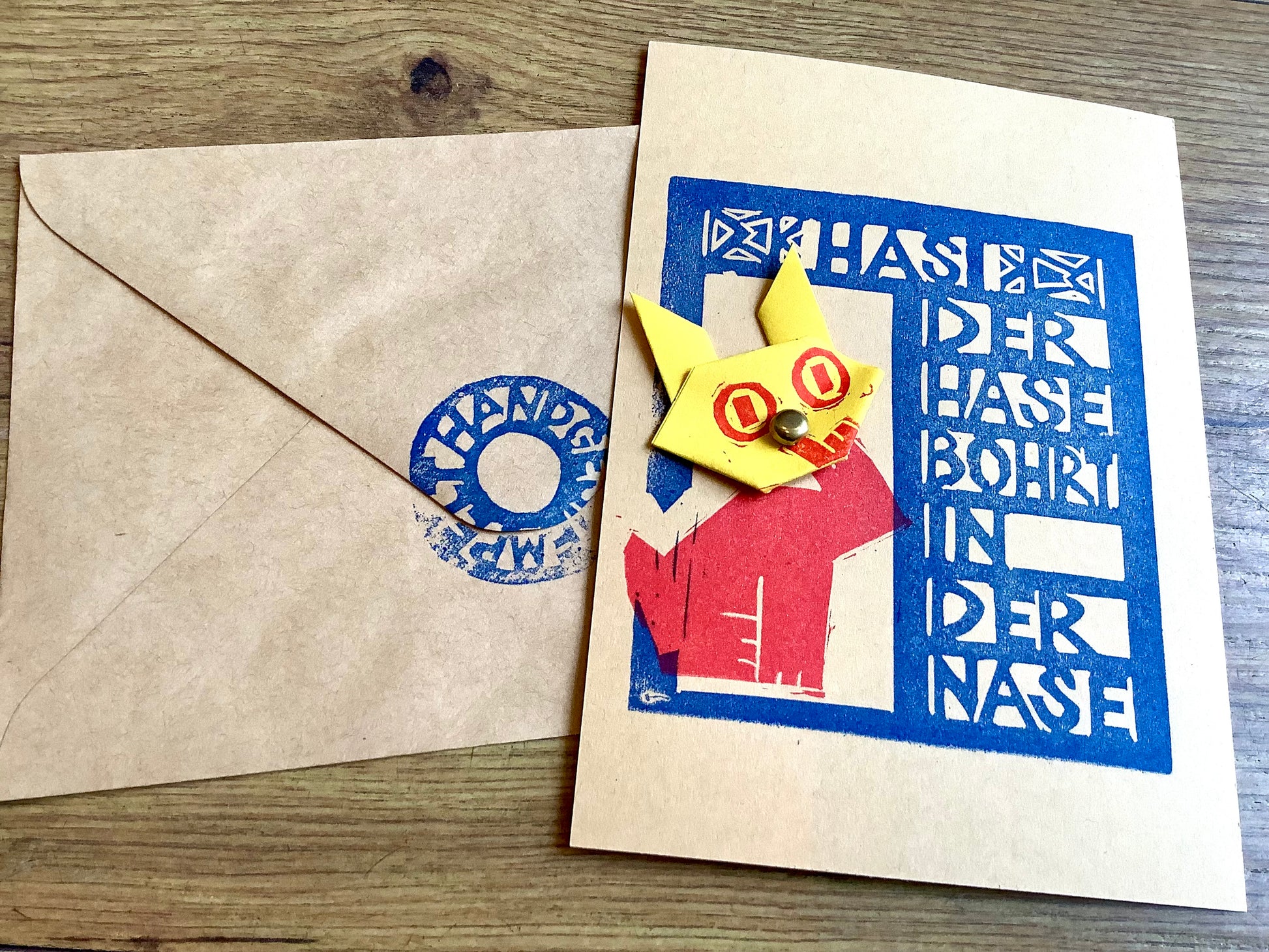 Postkarte mit angeheftetem Hasenkopf, aus Papier gefaltet. Text: Hasi der Hase bohrt in der Nase. Flitzpost. Bei Polly Paper in Berlin