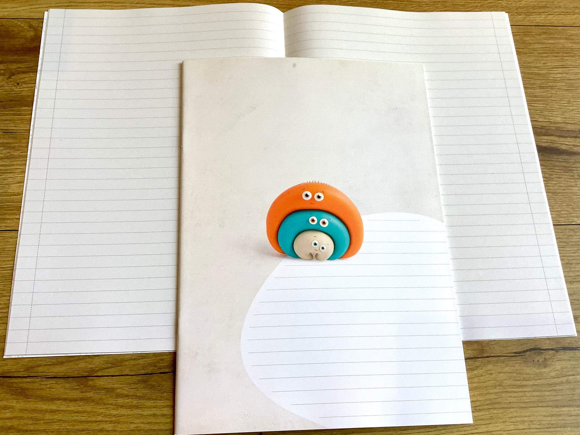 Ein liniertes Heft, das nicht nach Schule aussieht: süße bunte Knetfigur (Fantasiefigur) auf dem Cover. Weiß, liniert mit schmalem Rand, durch eine Linie abgetrennt.