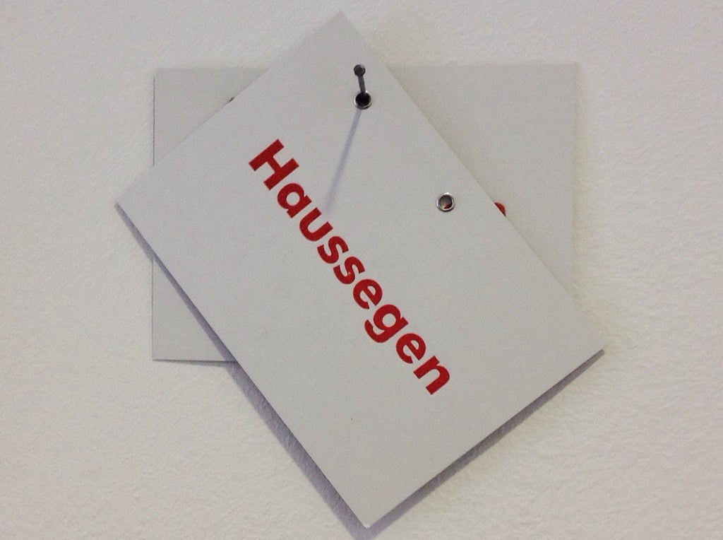 Postkarte "Haussegen" hängt schief am Nagel in einer von 2 Ösen zum Aufhängen