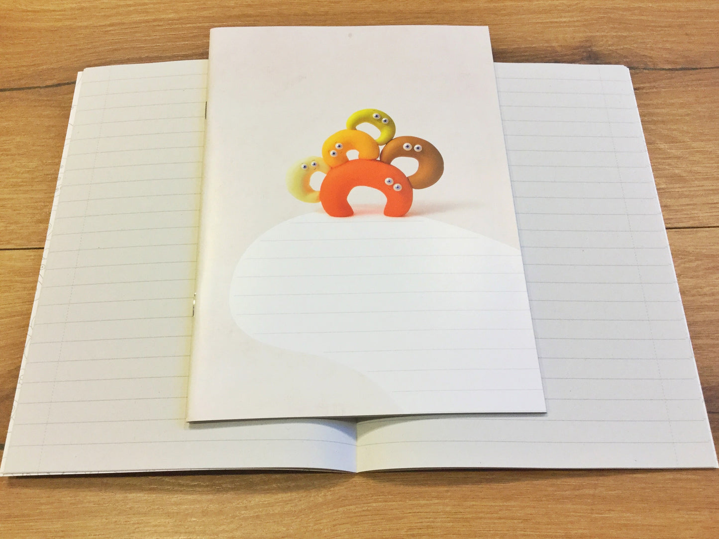 Ein liniertes Heft, das nicht nach Schule aussieht. Süße Knetfiguren auf dem Cover. 