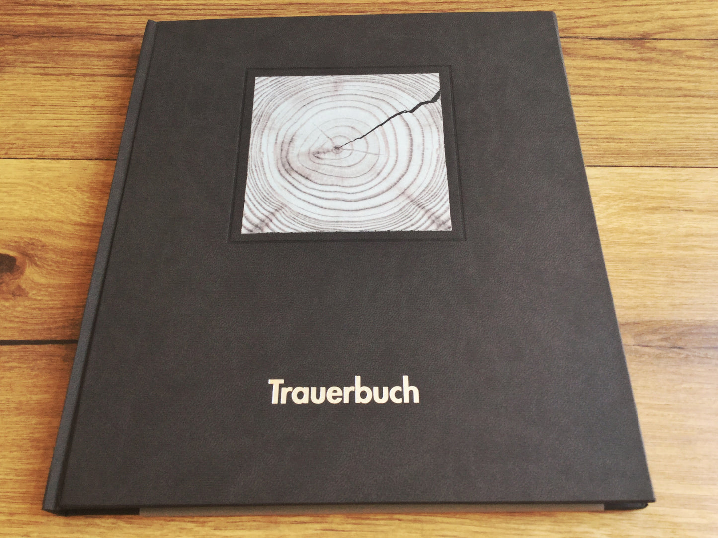 Schwarzes Trauerbuch mit einem quadratischen schwarz-weiß-Bild oben, das Baumringe zeigt. Silberner Aufdruck: Trauerbuch.