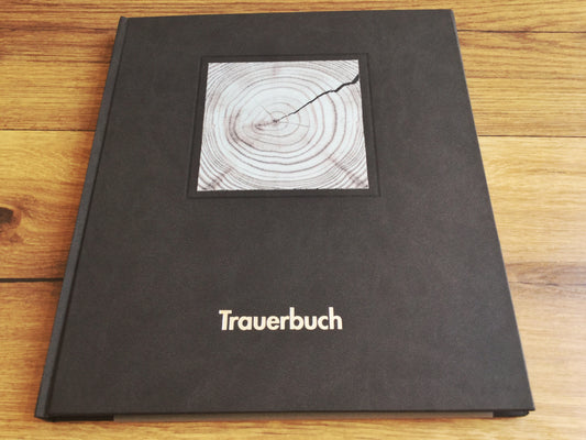 Schwarzes Trauerbuch mit einem quadratischen schwarz-weiß-Bild oben, das Baumringe zeigt. Silberner Aufdruck: Trauerbuch.